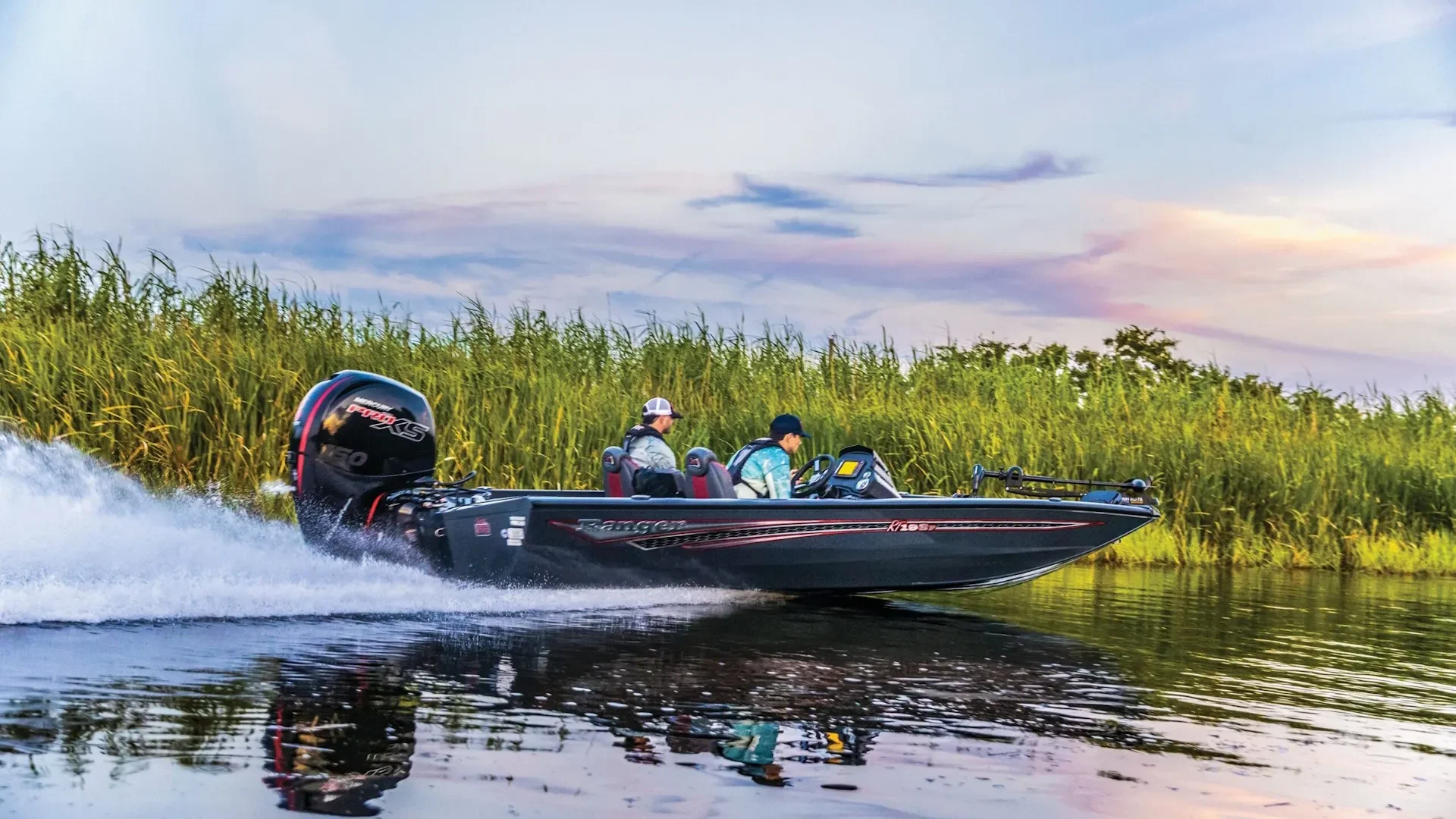 Ranger3-2nd-scaled A grey and black Ranger RT188P bass boat with a Mercury Pro XS motor, carrying two passengers at high speed on a river at sunset.
