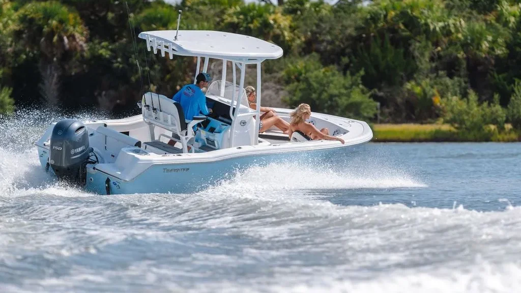 Tidewater2 A light blue Tidewater center console boat with a white T-top and a Yamaha outboard motor, carrying three passengers through choppy blue water.